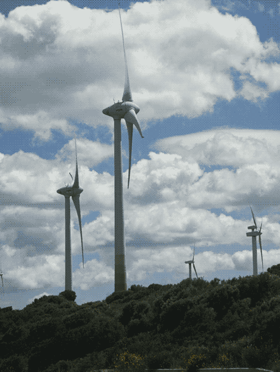 4 large wind turbines atop a hill, stretching up to the skies above. 2 are closer, fully visible, and 2 further away with the tops just visible over the hill. Bright blue skies with fluffy clouds fill most of the frame behind the turbines.